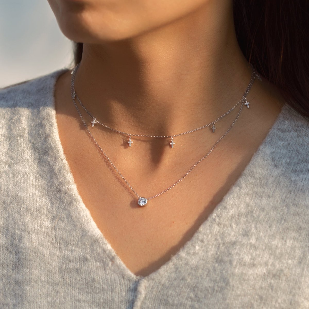 Sterling silver necklace with tiny dangling cross charms, layered over a solitaire, shown on a model
