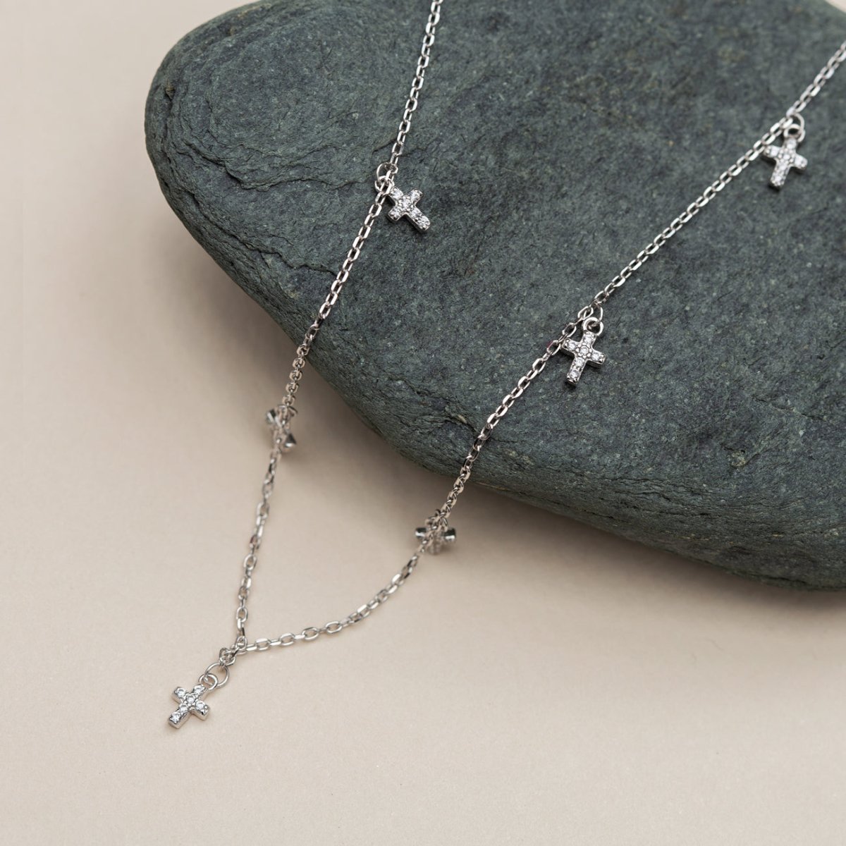 Sterling silver pavé zirconia cross-charm anklet draped over a grey stone
