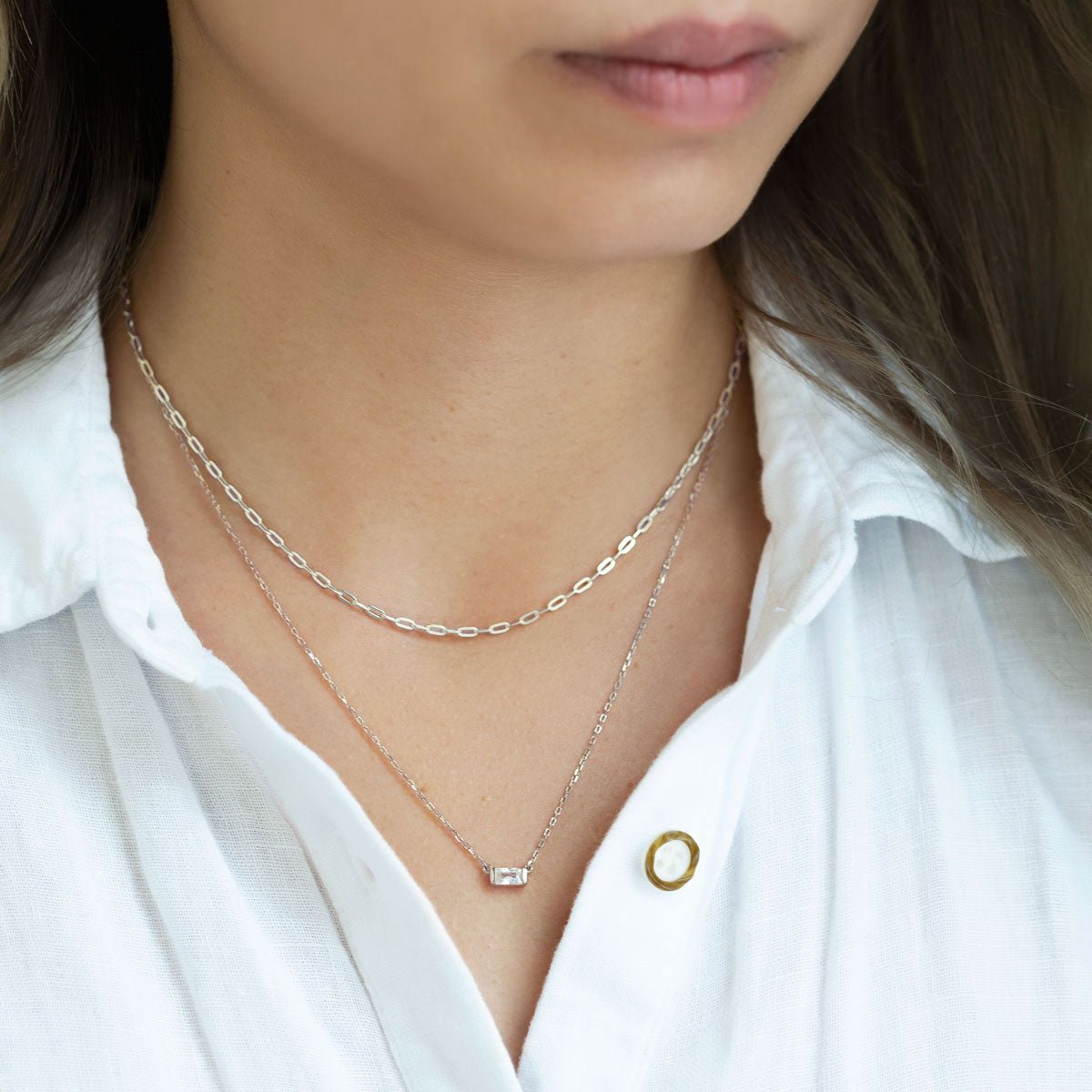 Sterling silver link chain necklace layered with a clear stone pendant, shown on a model's neckline