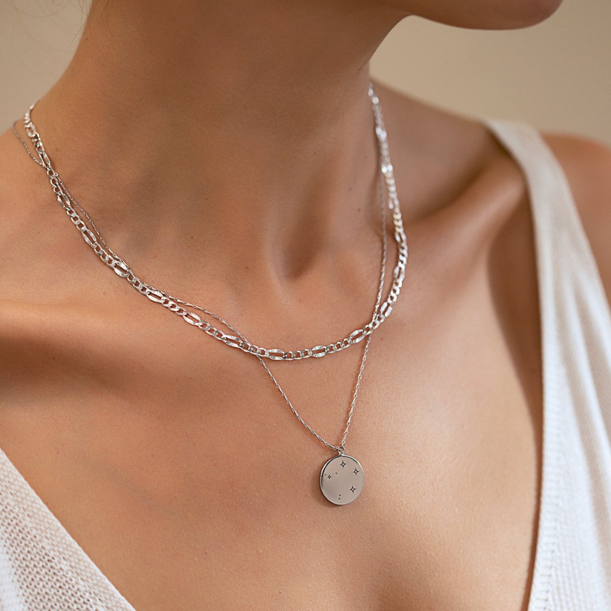 Sterling silver round constellation disc necklace layered with a chain, shown on a model's neckline