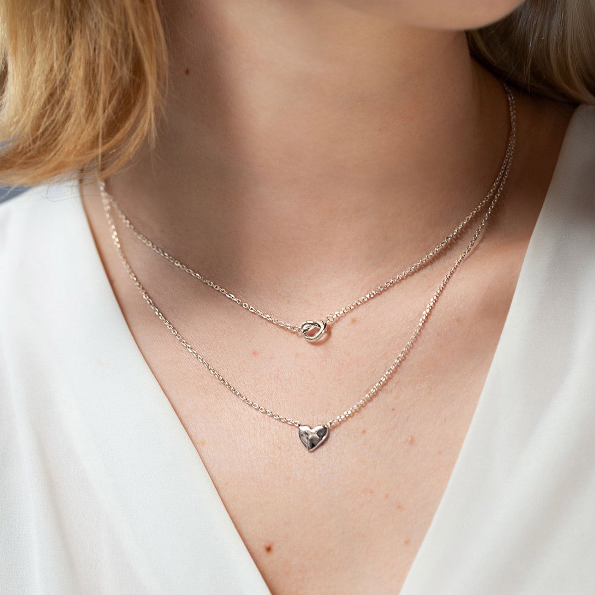 Sterling silver puffed heart pendant on a fine chain, shown layered on a model's neckline