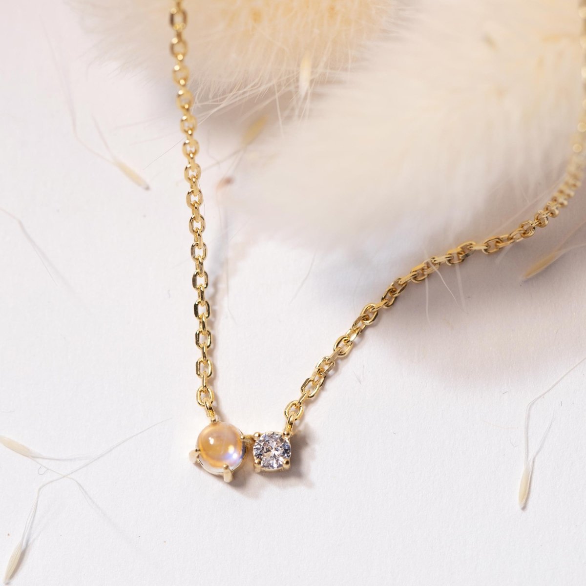 Gold vermeil necklace pendant pairing a moonstone with a clear stone, close-up on cream fur