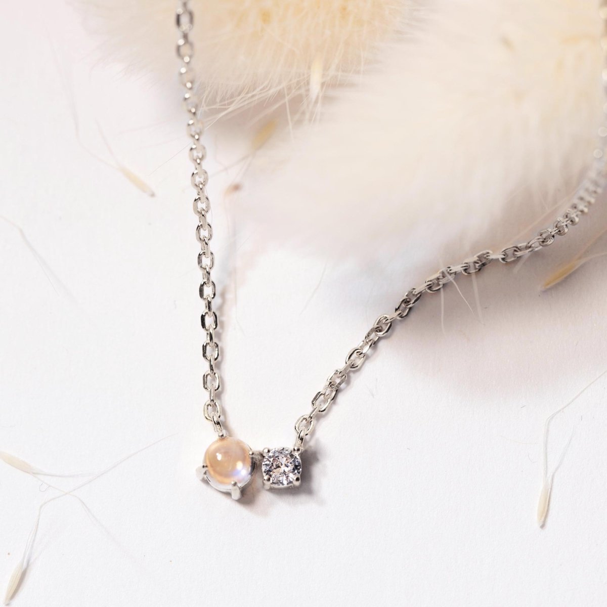 Sterling silver necklace pendant pairing a moonstone with a clear stone, close-up detail on cream fur