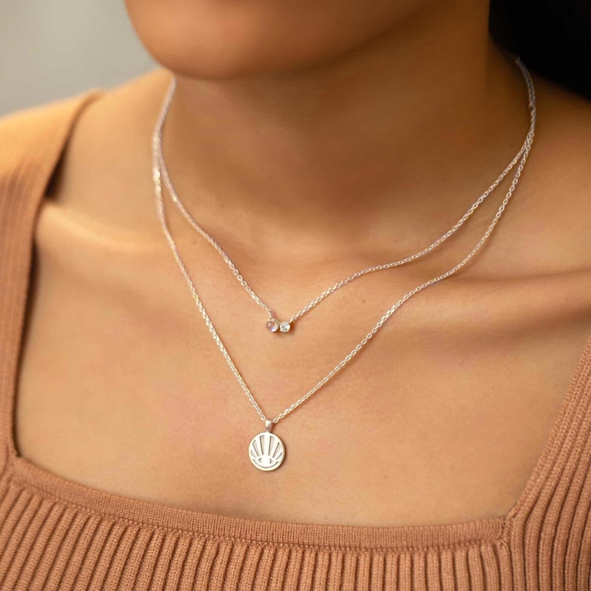 Sterling silver two-stone duet necklace with a moonstone and clear stone, on a model's neckline