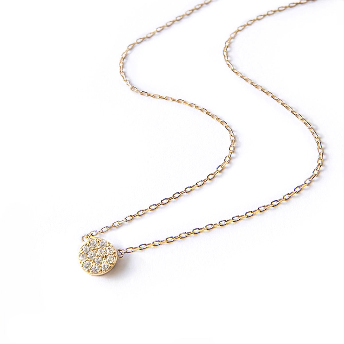 Gold vermeil layered necklace duo with a round pavé disc pendant set with clear stones, on a white background