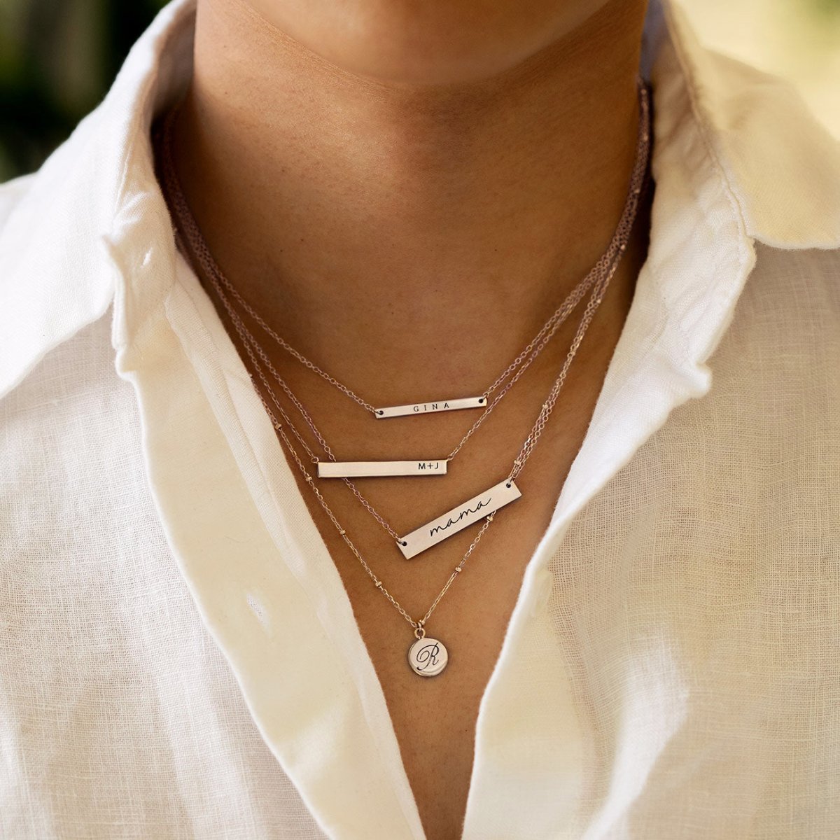 Rose gold vermeil bar and disc necklaces engraved with names and an initial, layered on a model's neckline