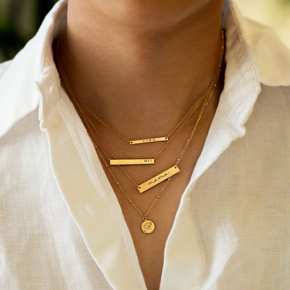 Gold vermeil bar and disc necklaces engraved with names and an initial, layered on a model's neckline
