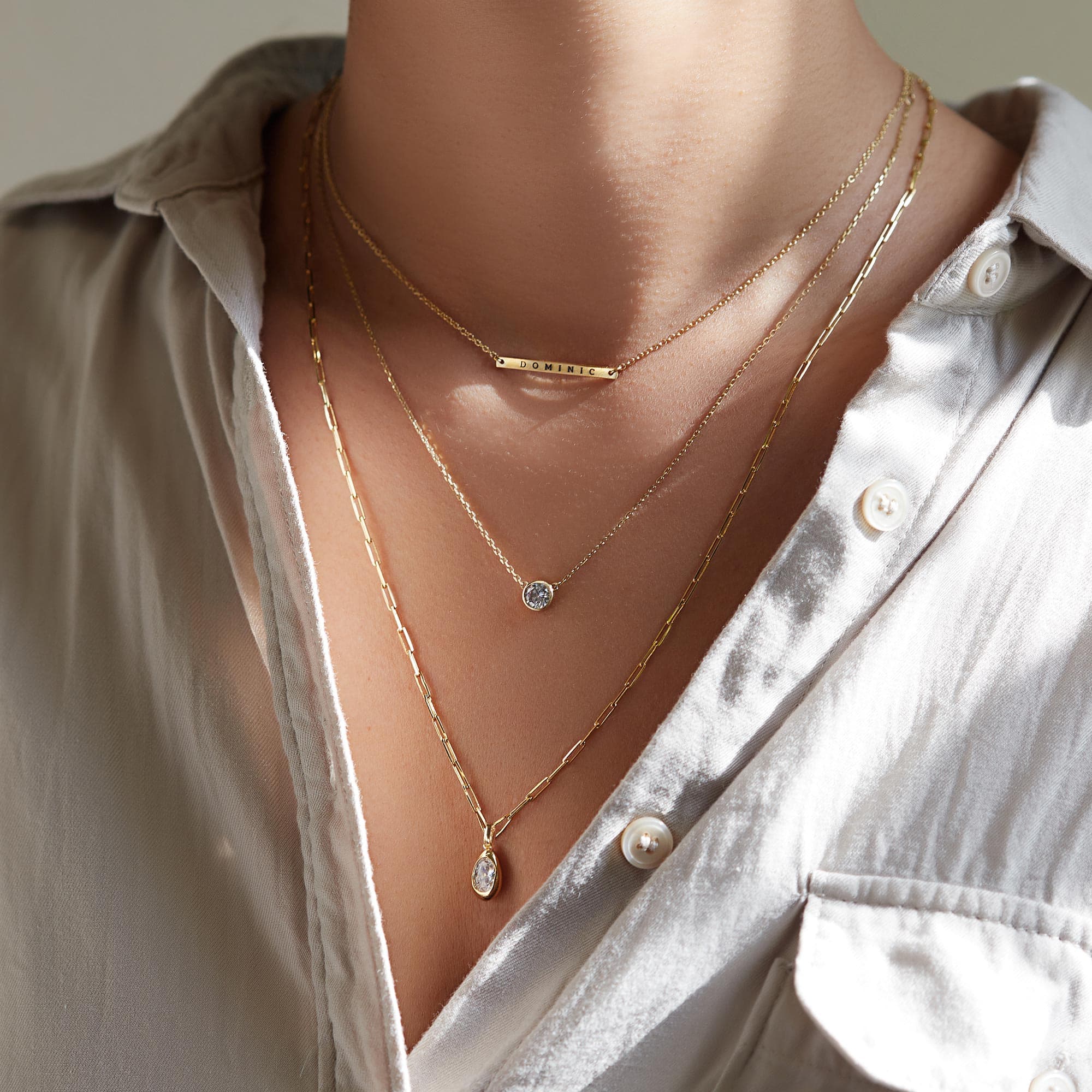 Gold layered necklaces with a clear-stone solitaire, a teardrop pendant and an engraved bar