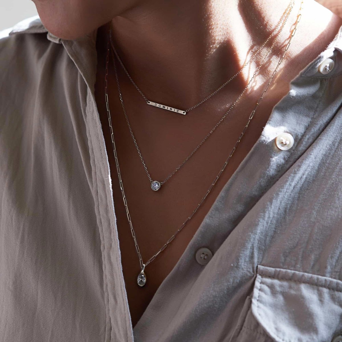 Silver layered necklaces with a bar engraved with a name, a clear-stone drop and a teardrop