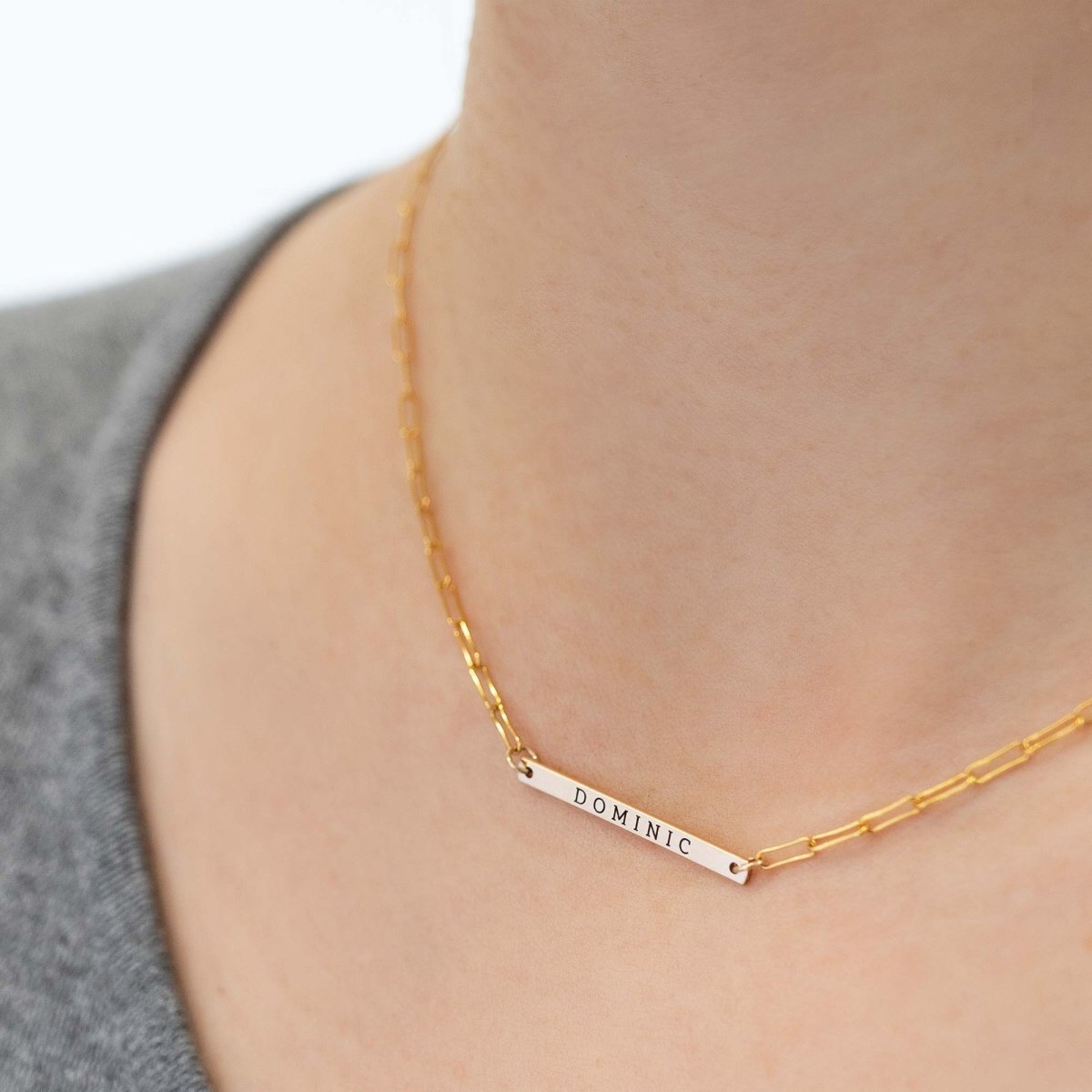 Gold-filled thin bar necklace engraved with a name, shown layered on a model's neckline