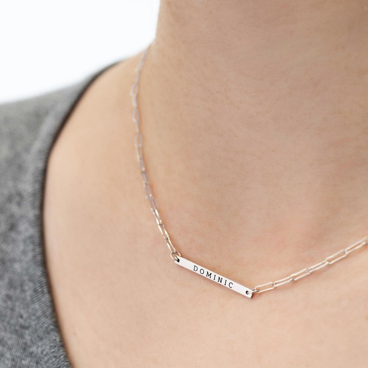 Sterling silver thin bar necklace engraved with a name, shown on a model's neckline