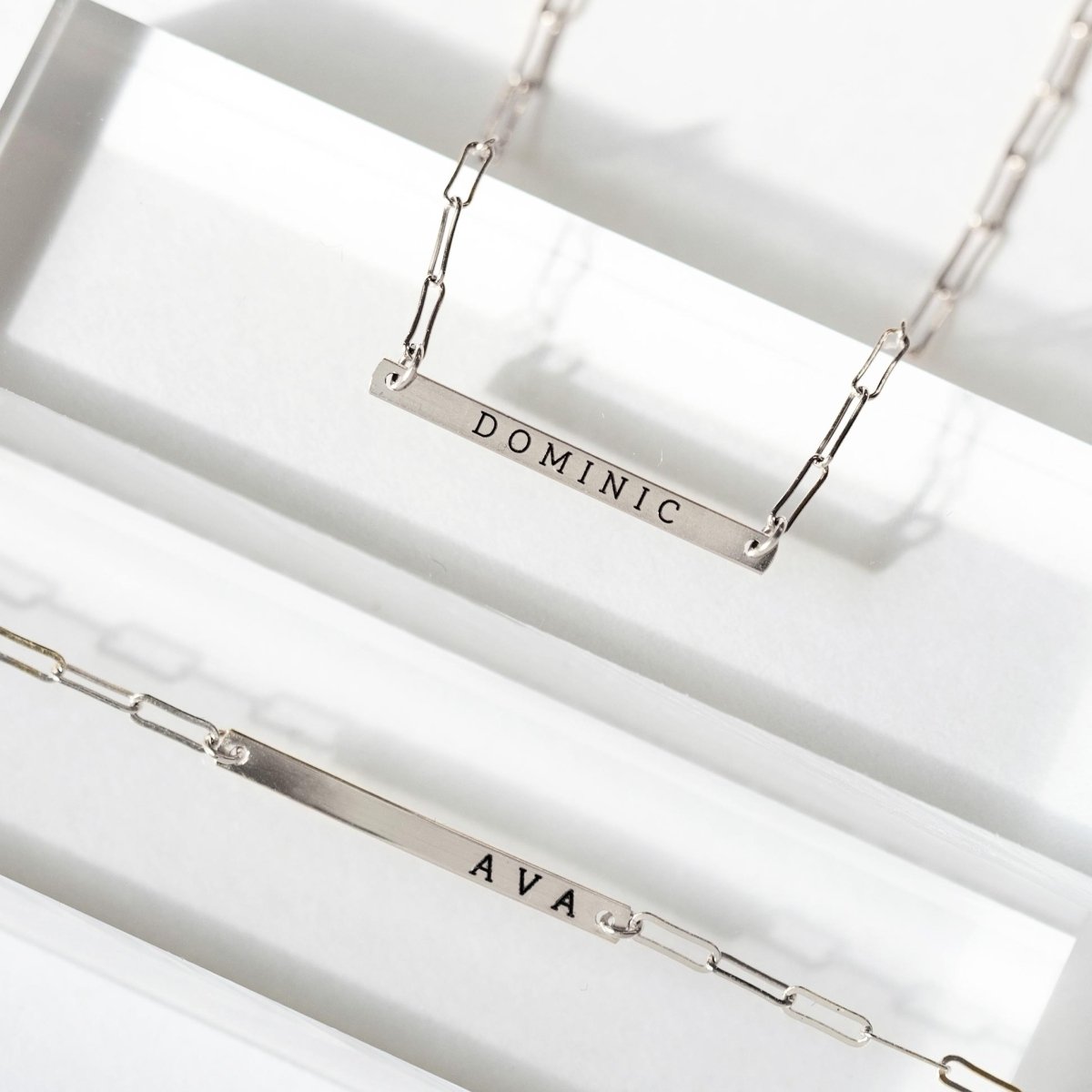 Two sterling silver thin bar paperclip chain necklaces engraved with names, shown on a white background