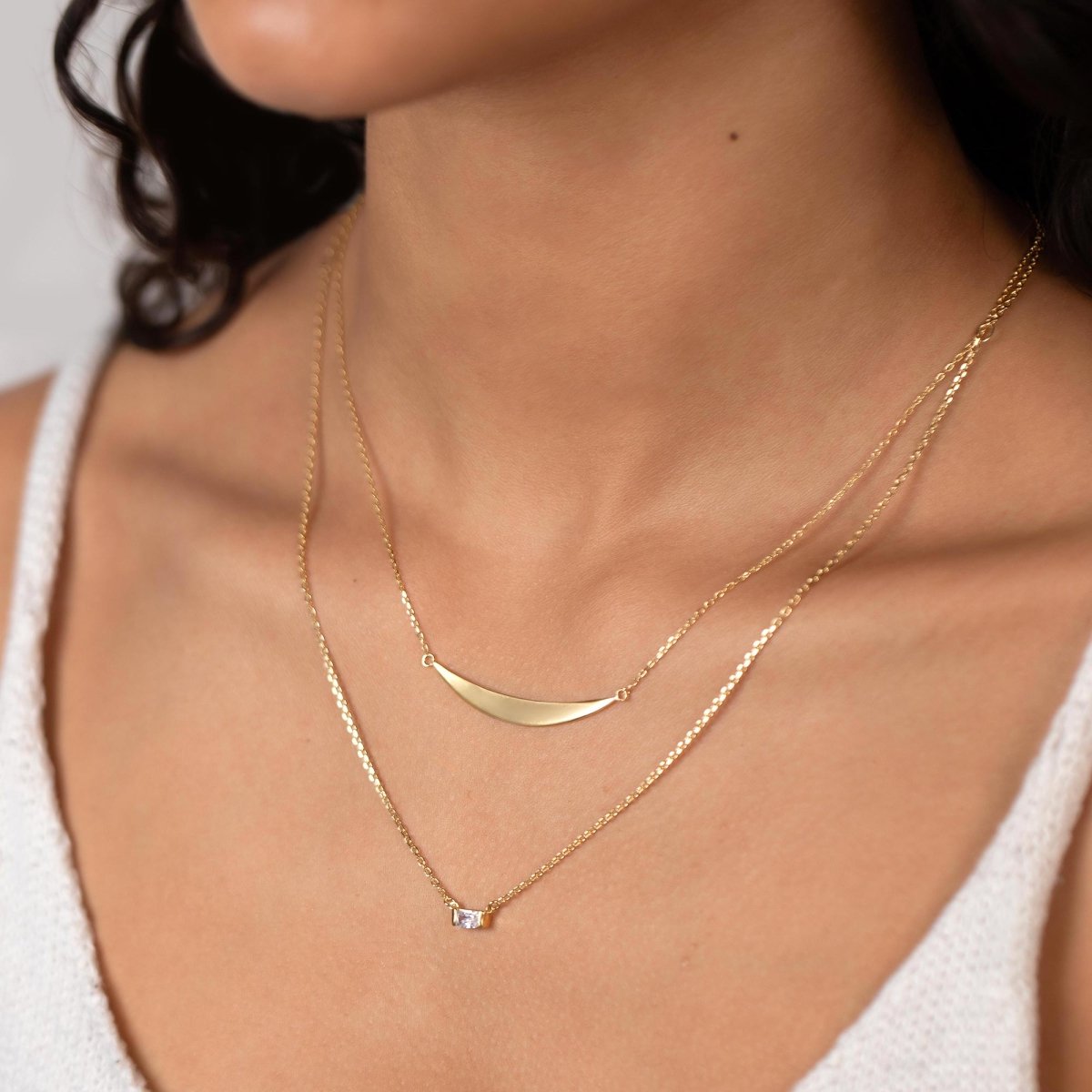 Gold vermeil baguette zirconia necklace with a small clear stone, shown layered on a model's neckline