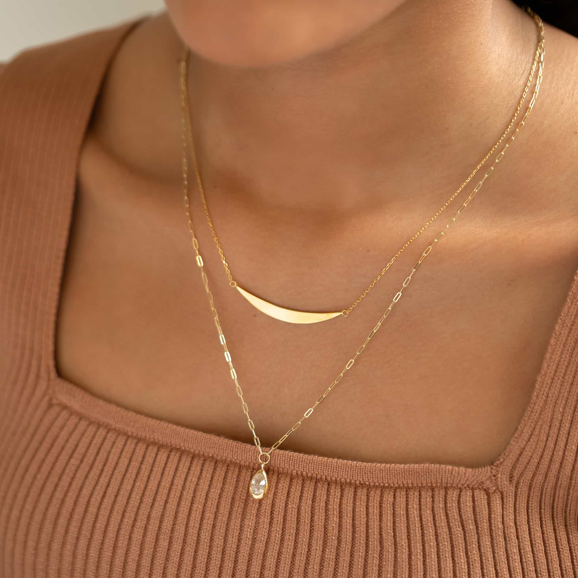 Gold vermeil crescent bar necklace on a model, layered above a chain with a clear teardrop stone