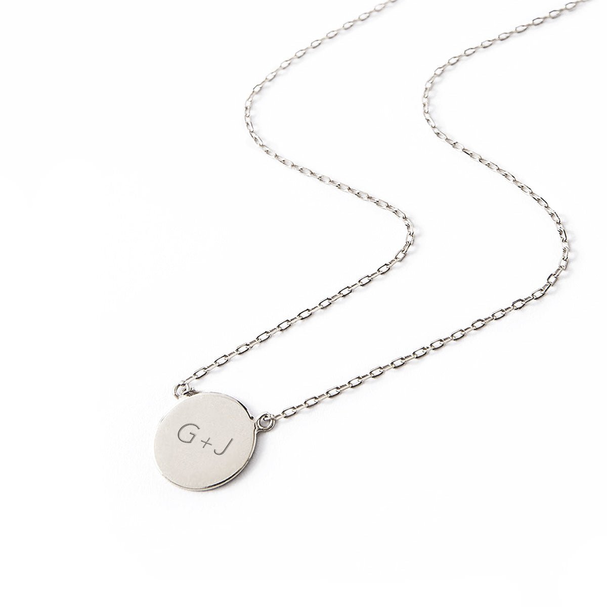 Sterling silver engravable disc necklace engraved with initials, laid on a white background