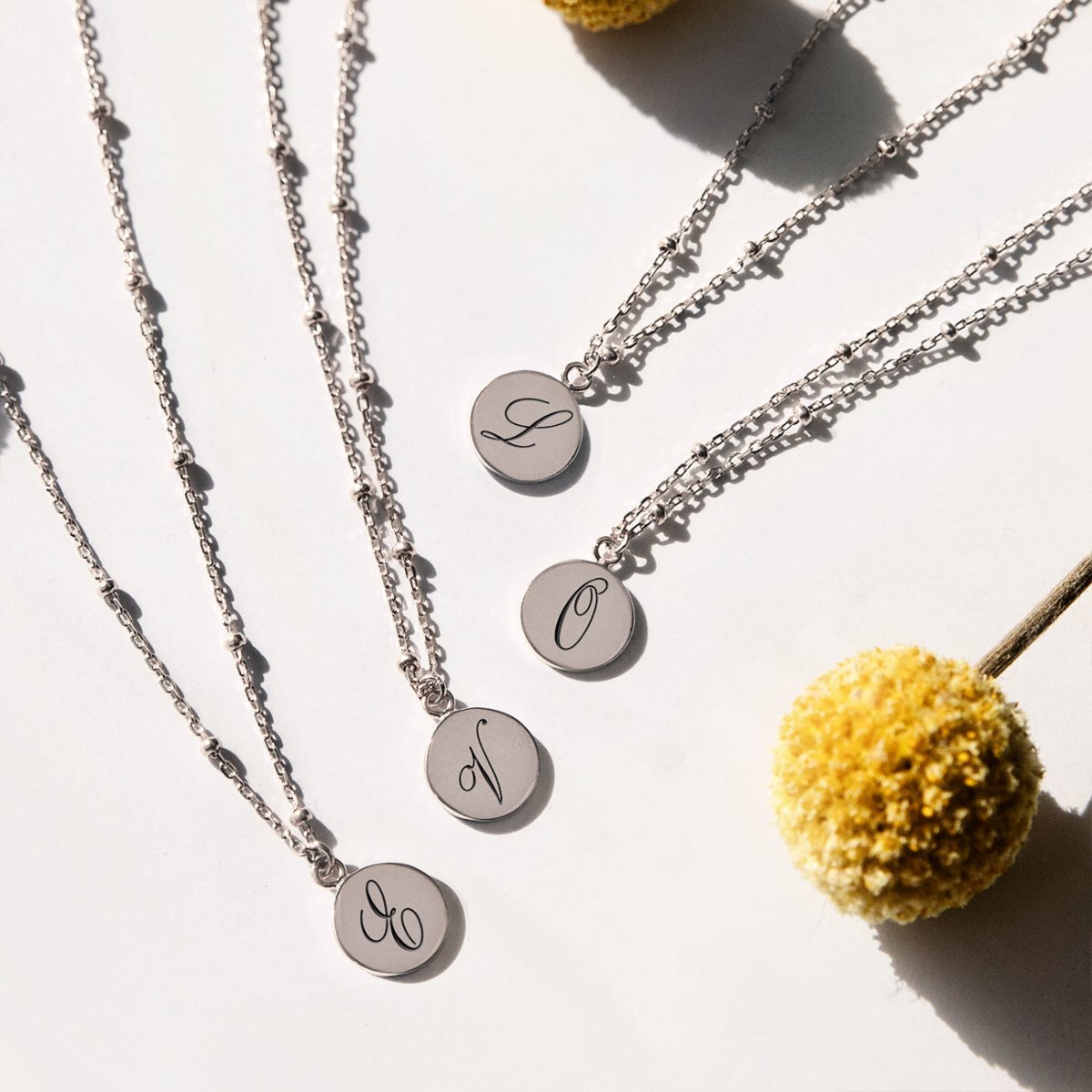 Sterling silver initial disc bead chain necklaces, each engraved with an initial, with a yellow bloom