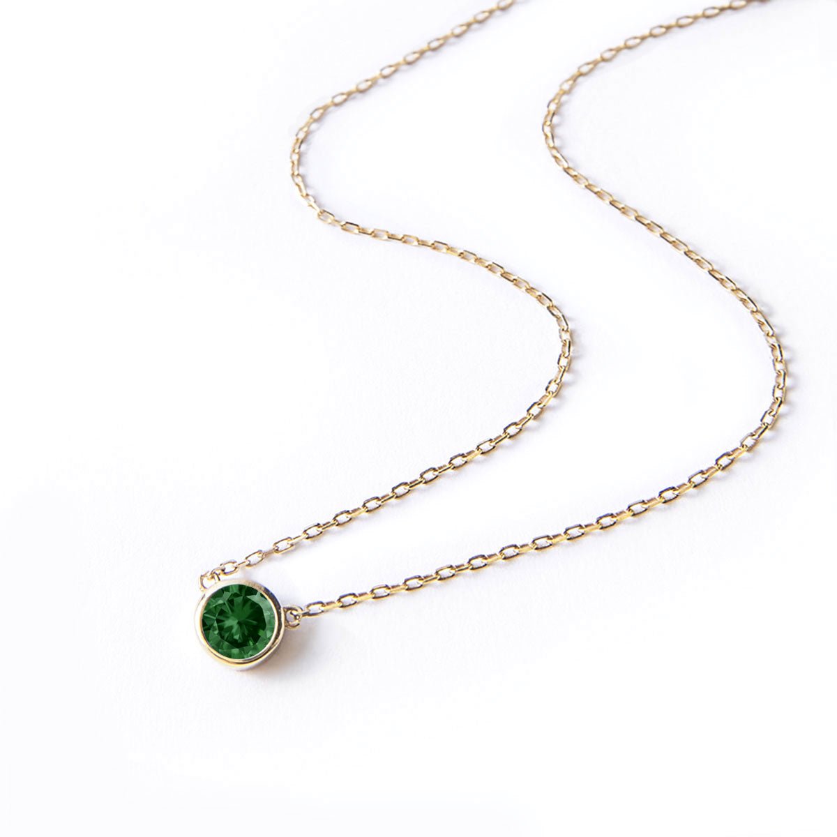 Gold vermeil solitaire necklace with a round green emerald pendant, laid on a white background