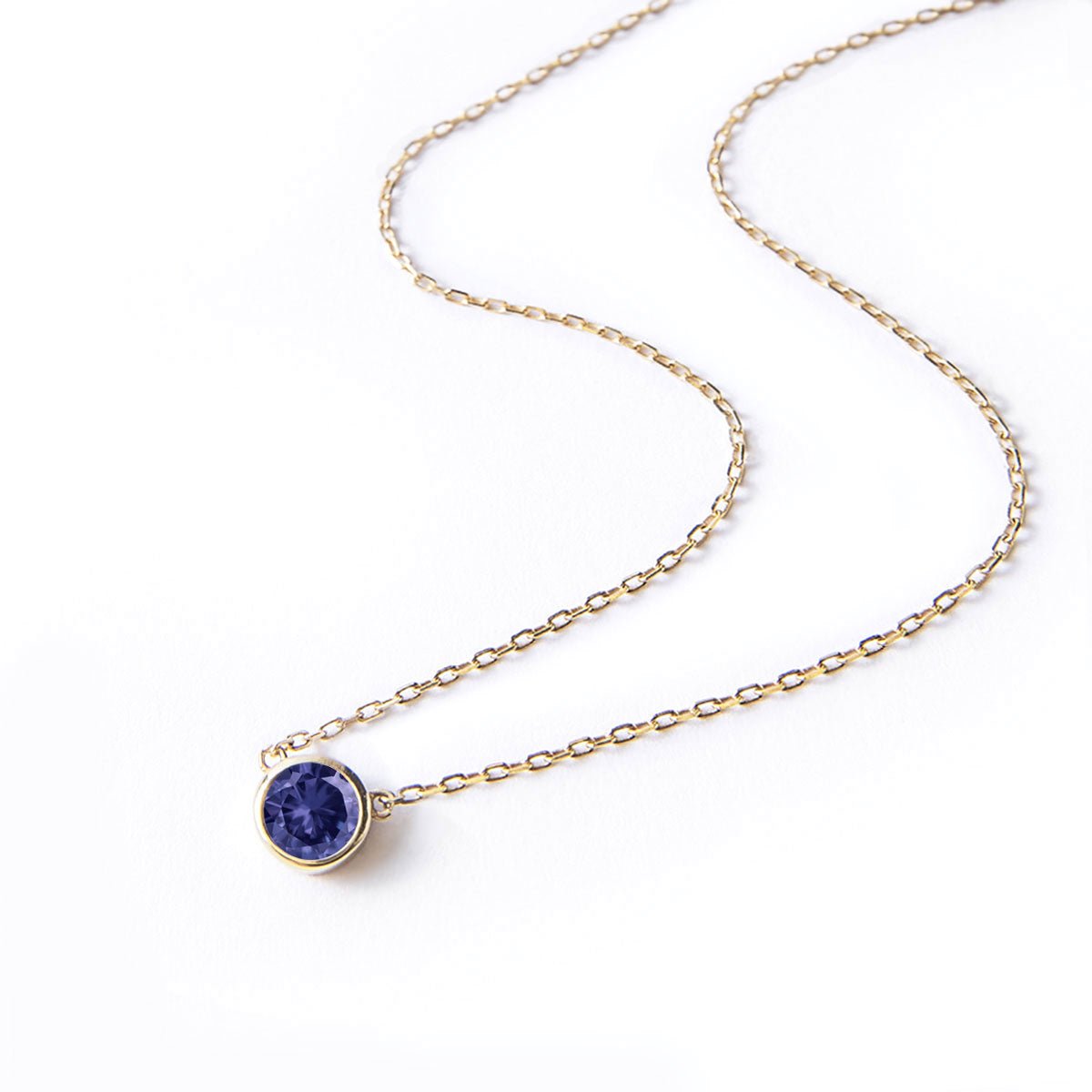 Gold vermeil solitaire necklace with a round bezel-set blue sapphire, on a white background