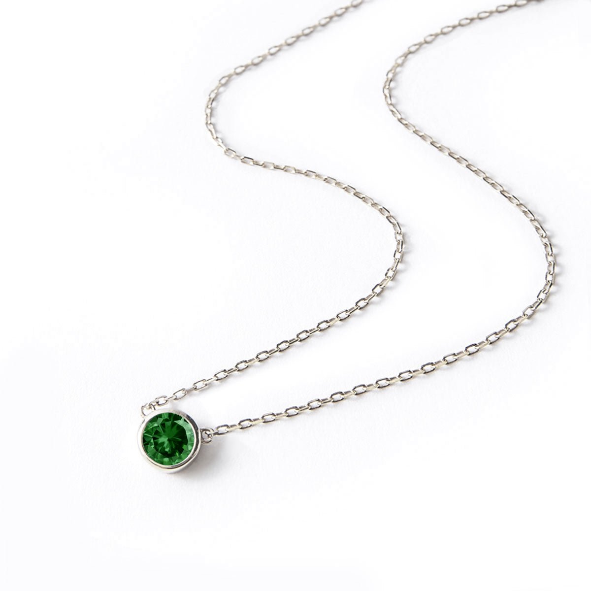 Sterling silver solitaire necklace with a round green emerald pendant, laid on a white background