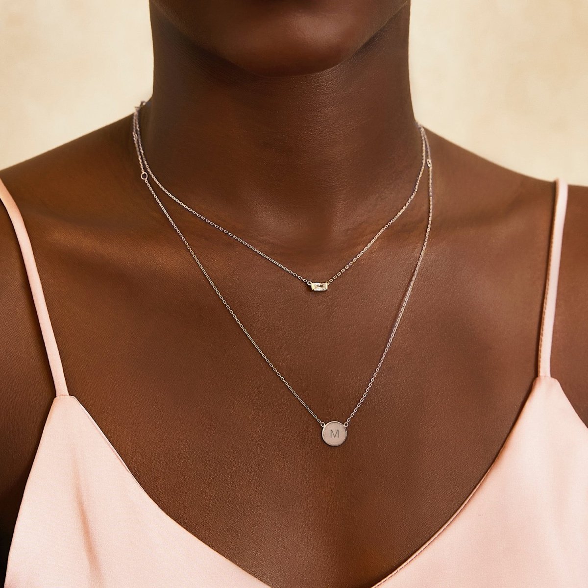 Sterling silver initial disc necklace engraved with an initial, layered and shown on a model's neckline