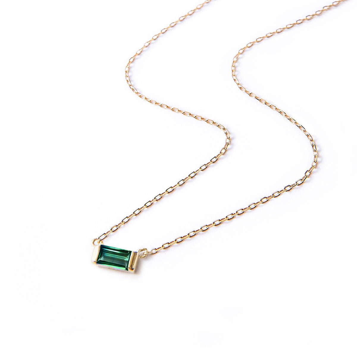 Gold vermeil necklace with a green emerald baguette pendant on a thin chain, laid on a white background