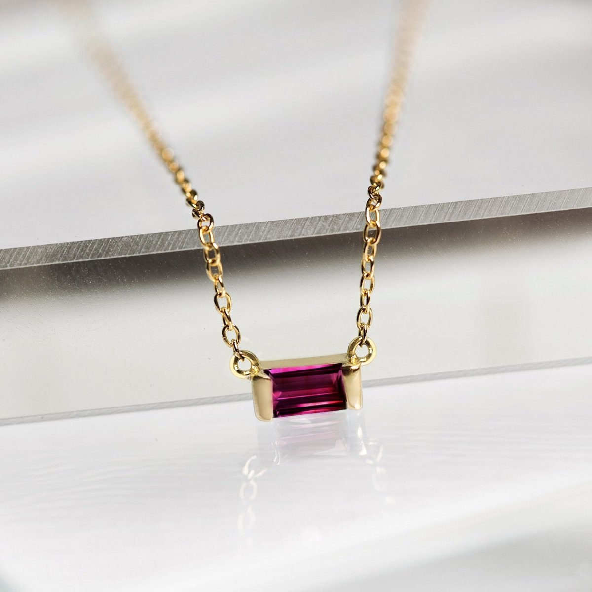 Gold vermeil ruby baguette pendant on a fine chain, close-up resting on a white surface