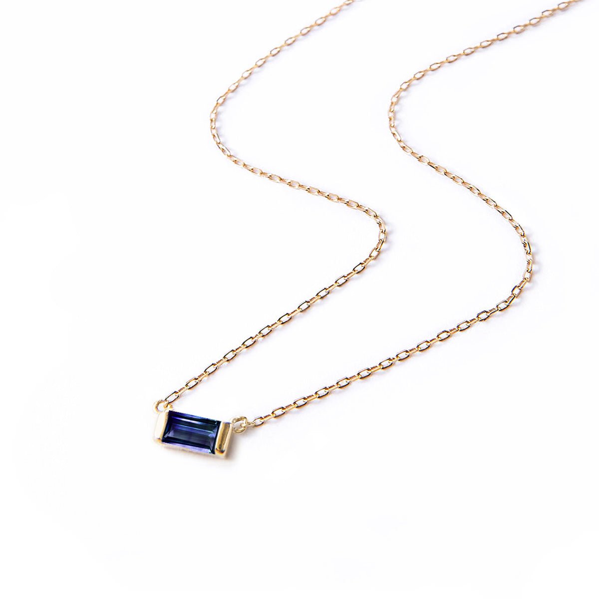 Gold vermeil baguette blue sapphire pendant on a fine chain, laid on a white background