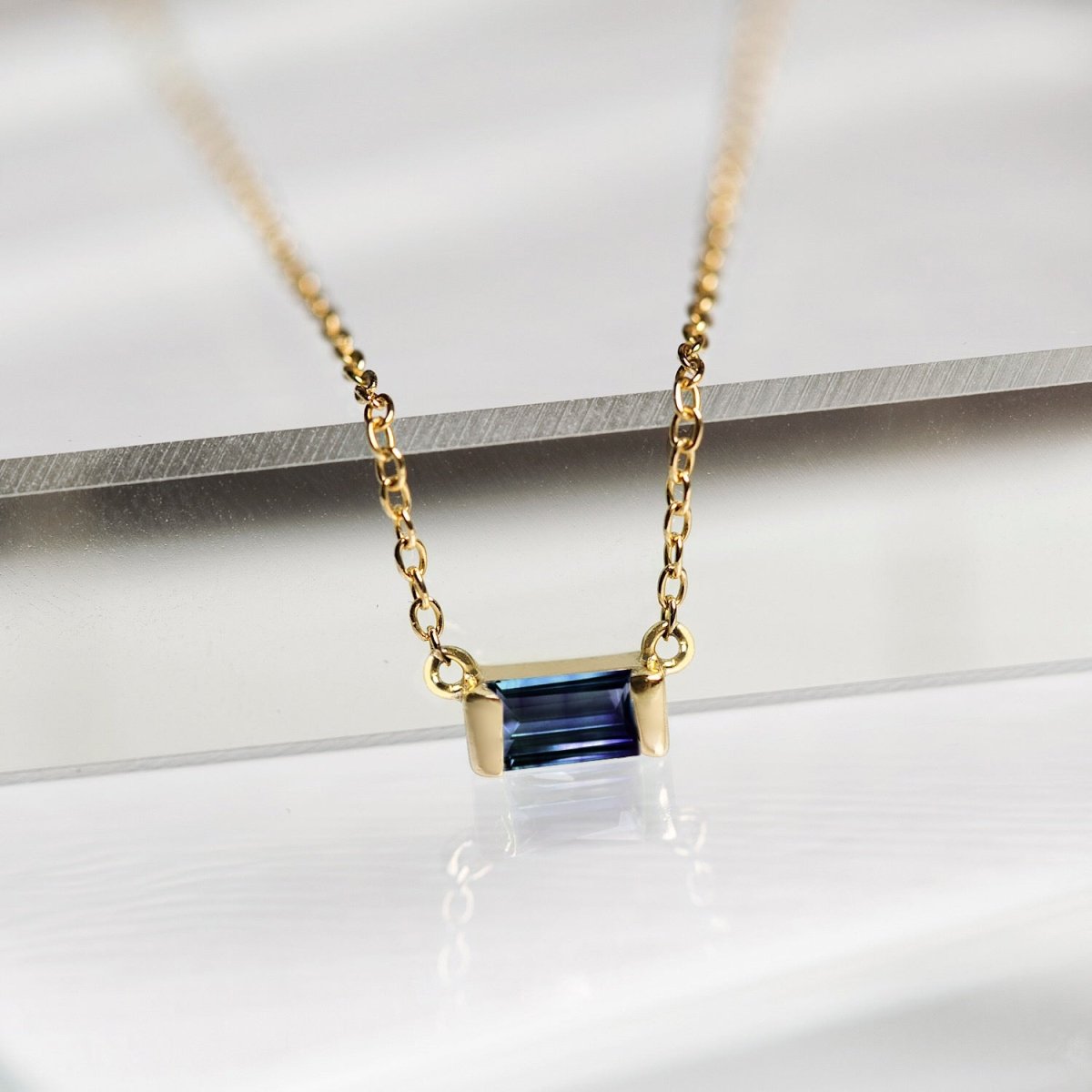 Gold vermeil baguette blue sapphire pendant, close-up detail resting on a white surface