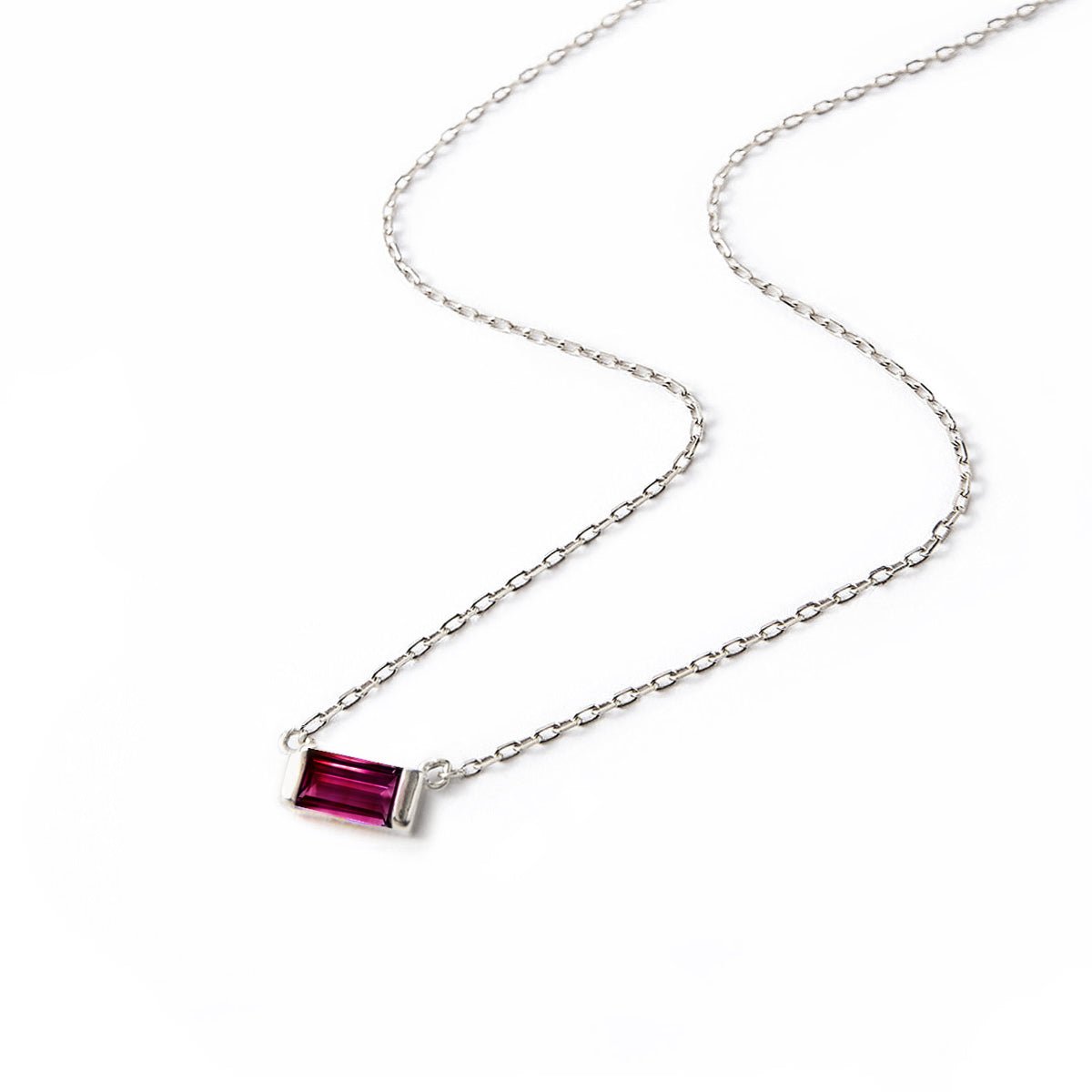 Sterling silver necklace with a red ruby baguette pendant on a thin chain, laid on a white background
