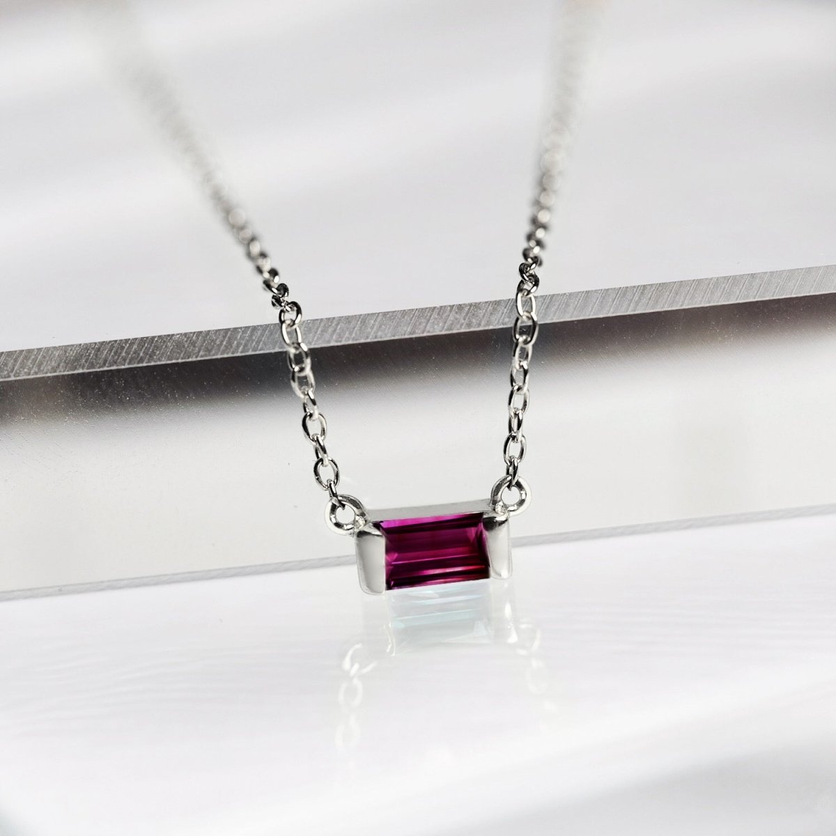 Sterling silver ruby baguette pendant on a fine chain, close-up resting on a white surface