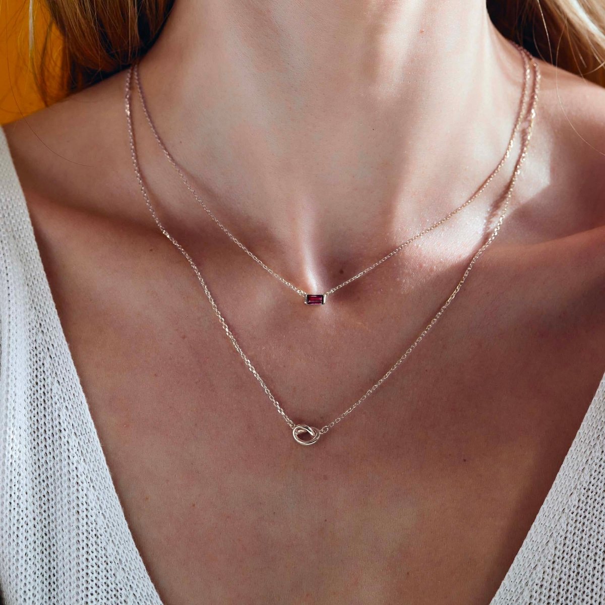 Sterling silver baguette ruby pendant layered with a loveknot necklace, shown on a model's neckline