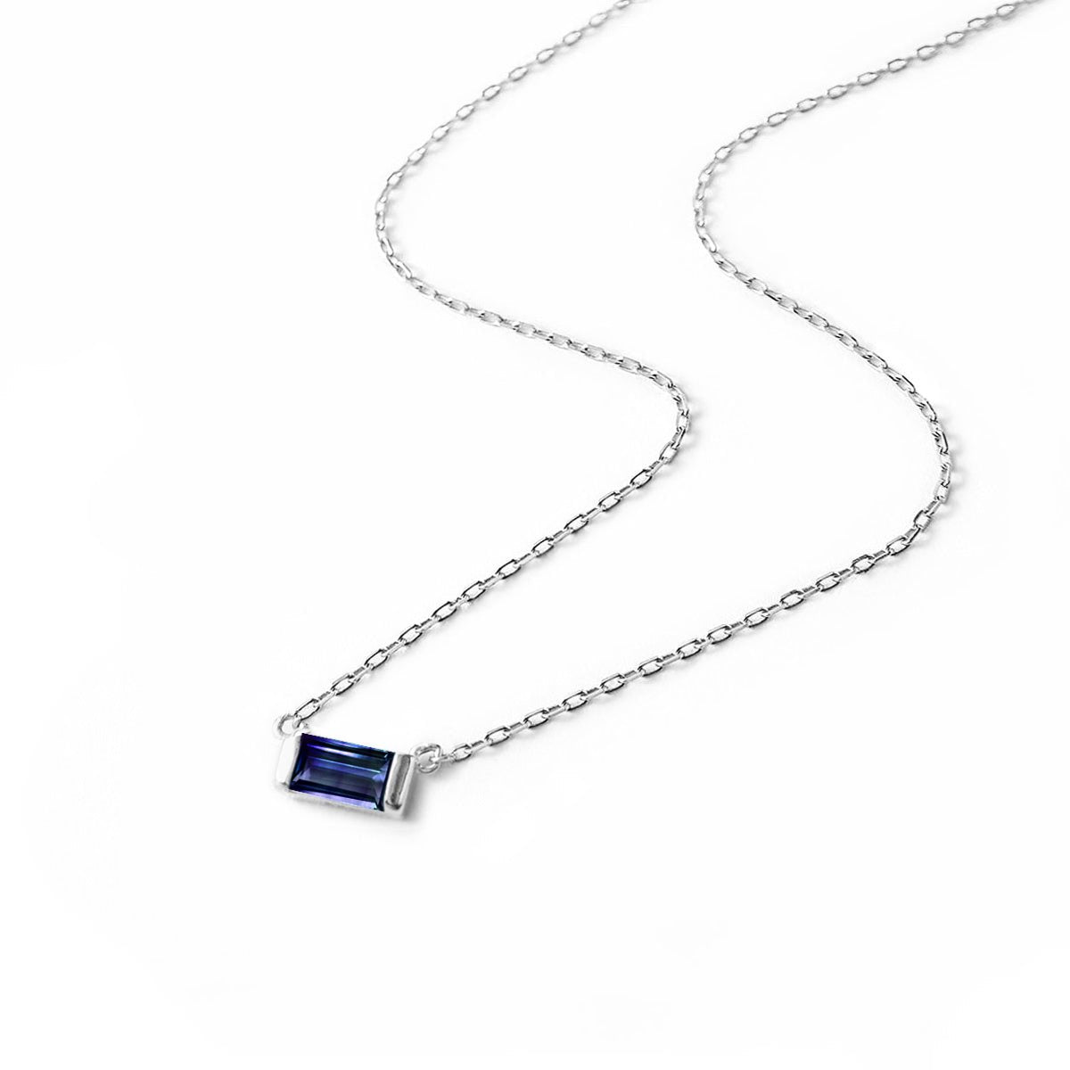 Sterling silver baguette blue sapphire pendant on a fine chain, laid on a white background