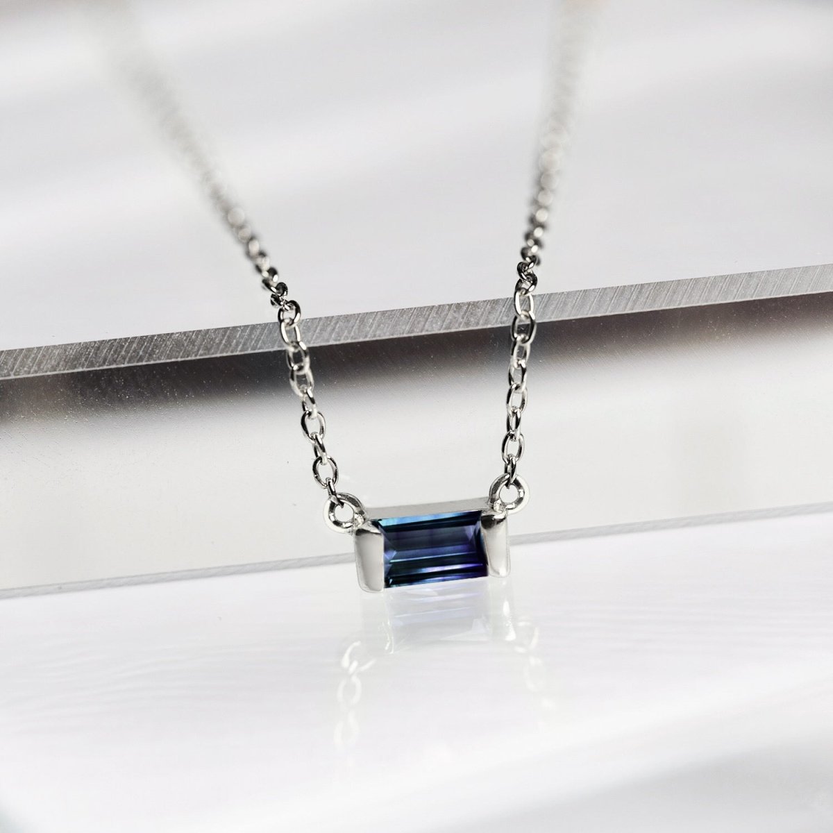 Sterling silver baguette blue sapphire pendant, close-up detail resting on a white surface