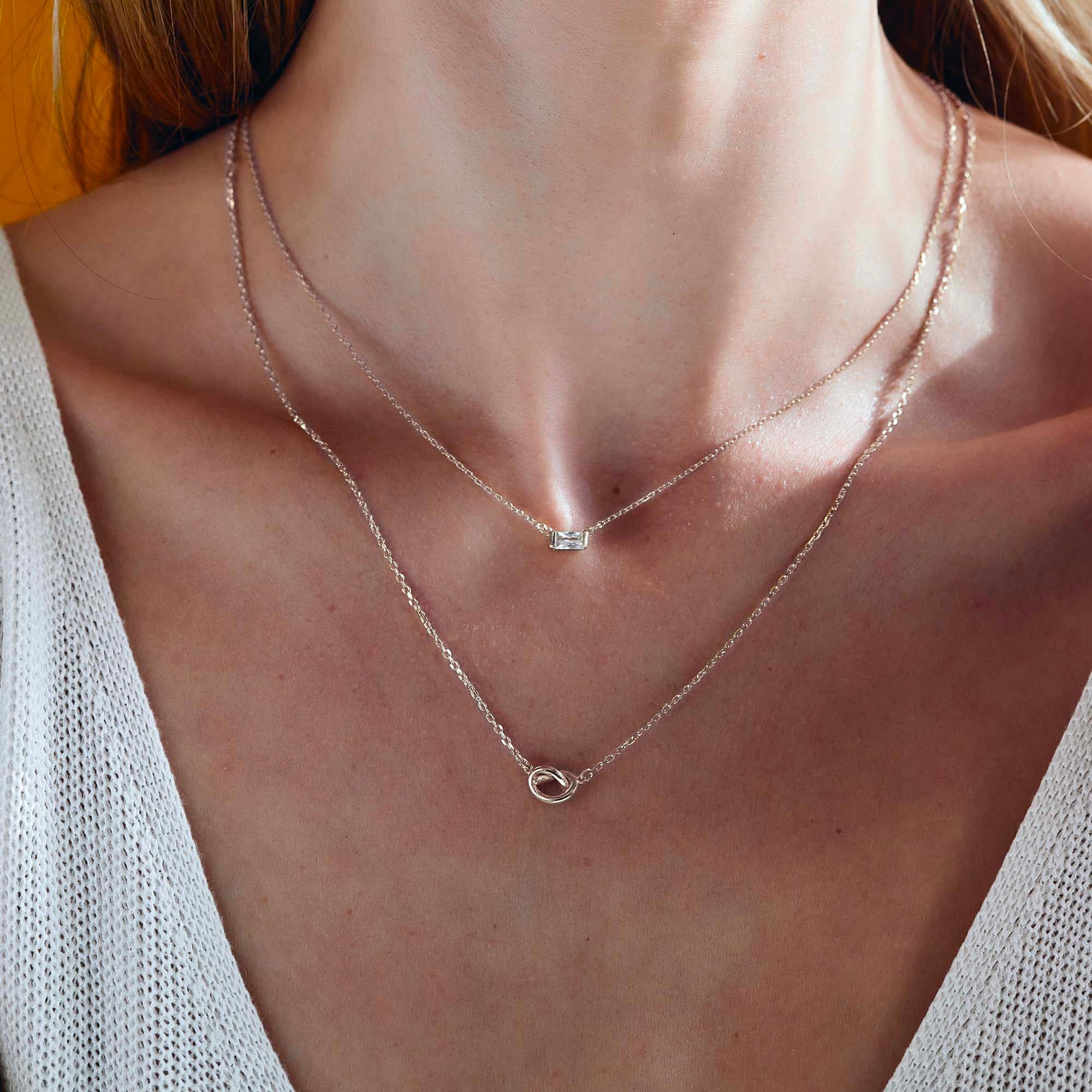 Sterling silver baguette white zirconia and loveknot layered necklaces, shown on a model's neckline