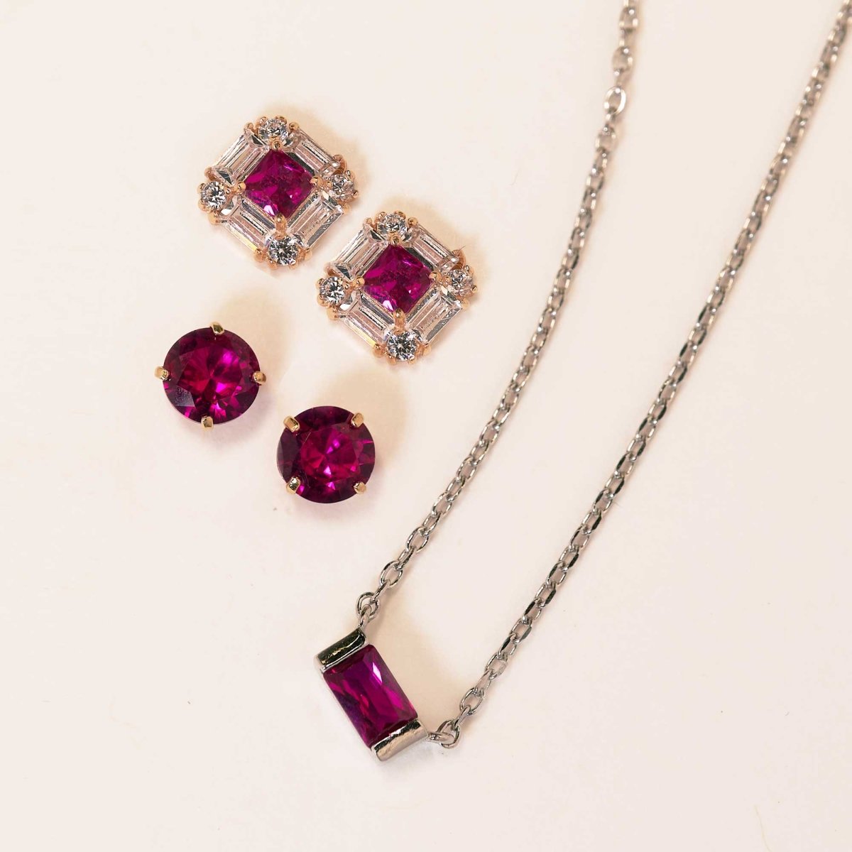 14K gold ruby halo studs, round ruby studs and a baguette ruby pendant on a white chain