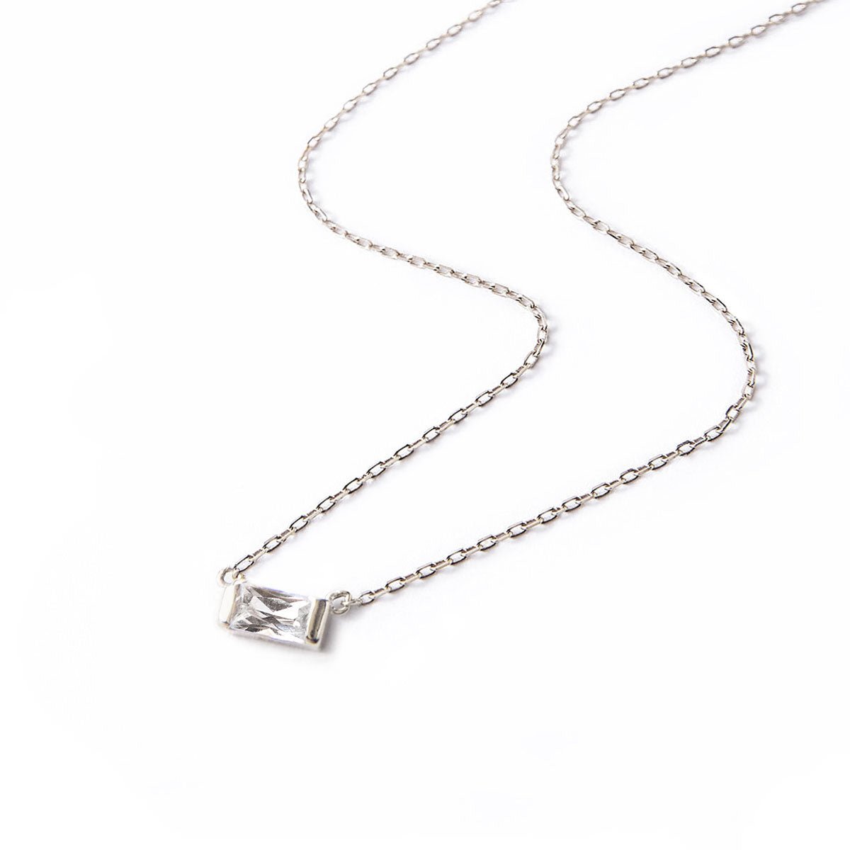 Sterling silver baguette necklace with a clear white zirconia pendant, laid on a white background