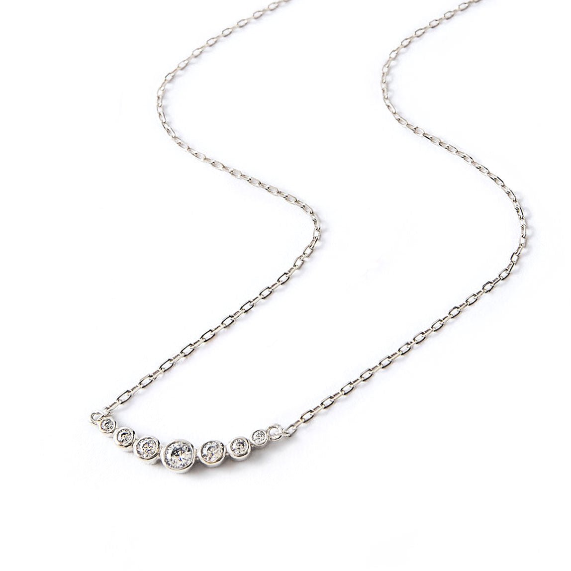 Sterling silver curved bar necklace with graduated round clear stones, laid on a white background