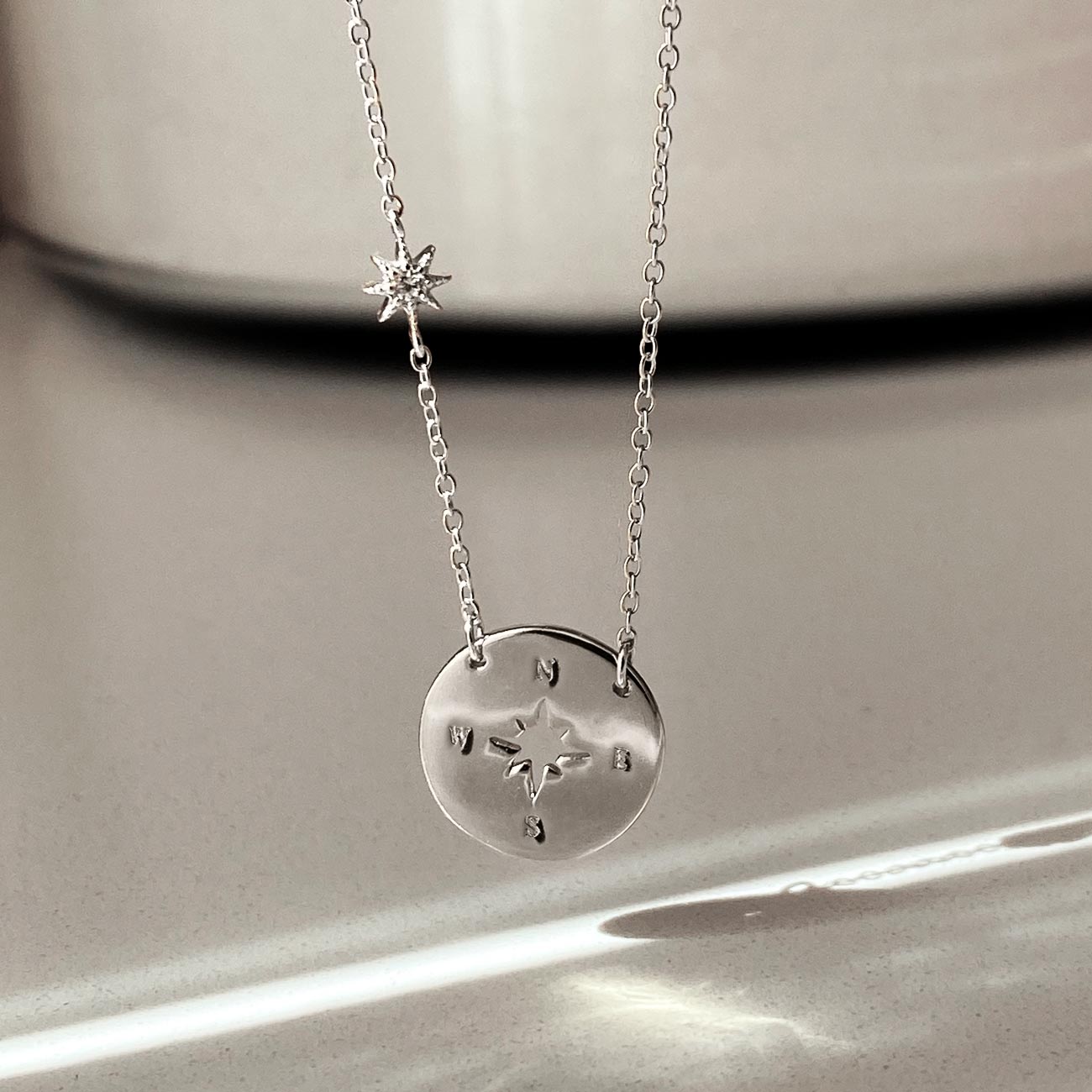 Sterling silver compass disc necklace with a star cutout and clear stone, hanging close-up detail