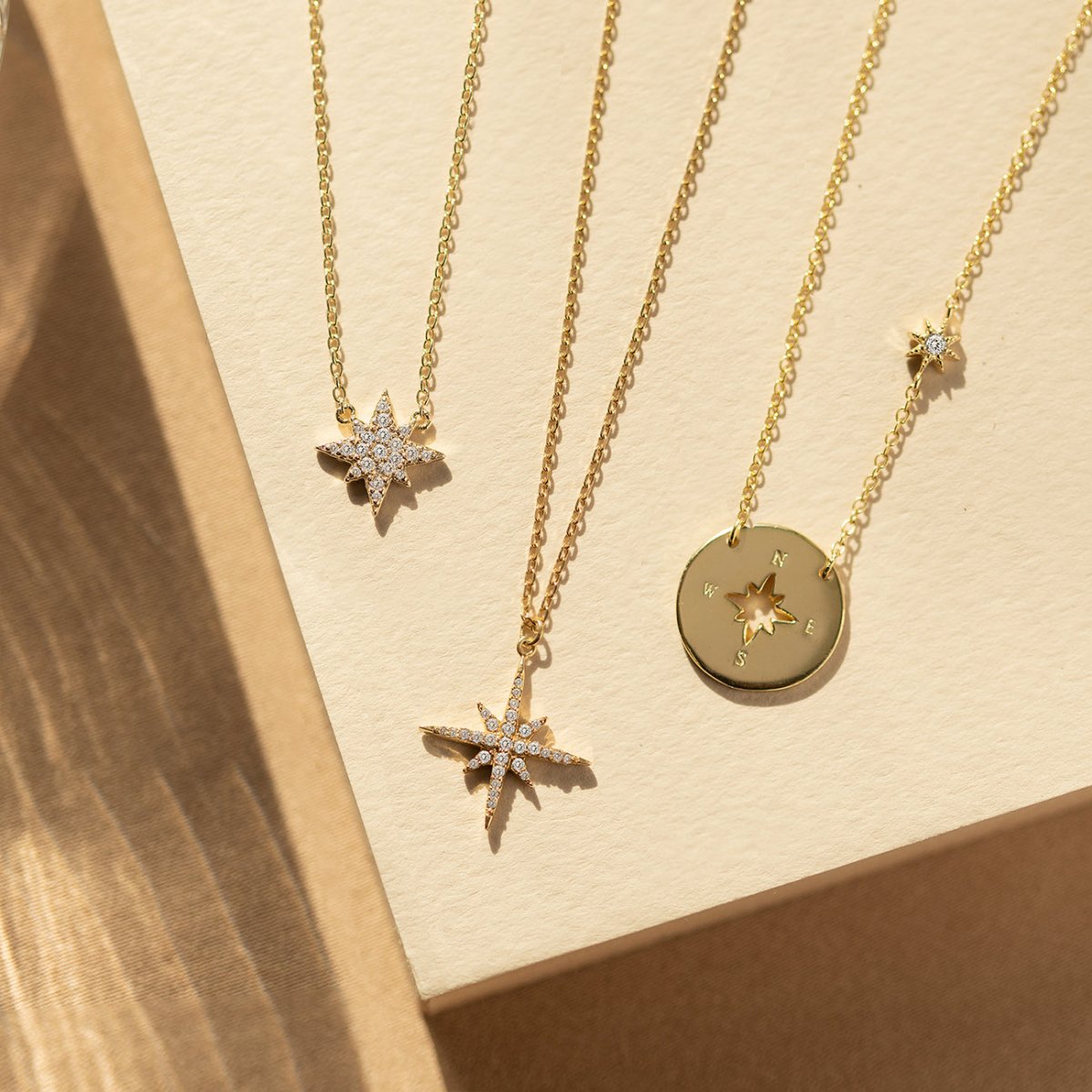 Gold vermeil compass disc and pavé starburst necklaces with clear stones, shown laid as a group