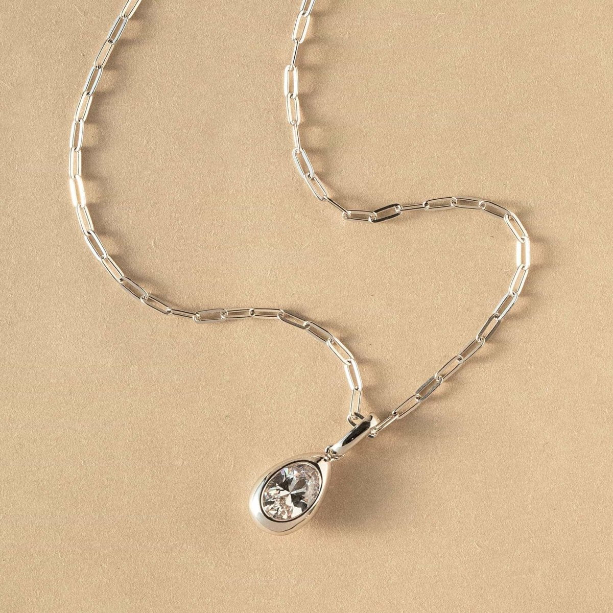 Sterling silver teardrop zirconia pendant on a paperclip chain, laid on a cream background