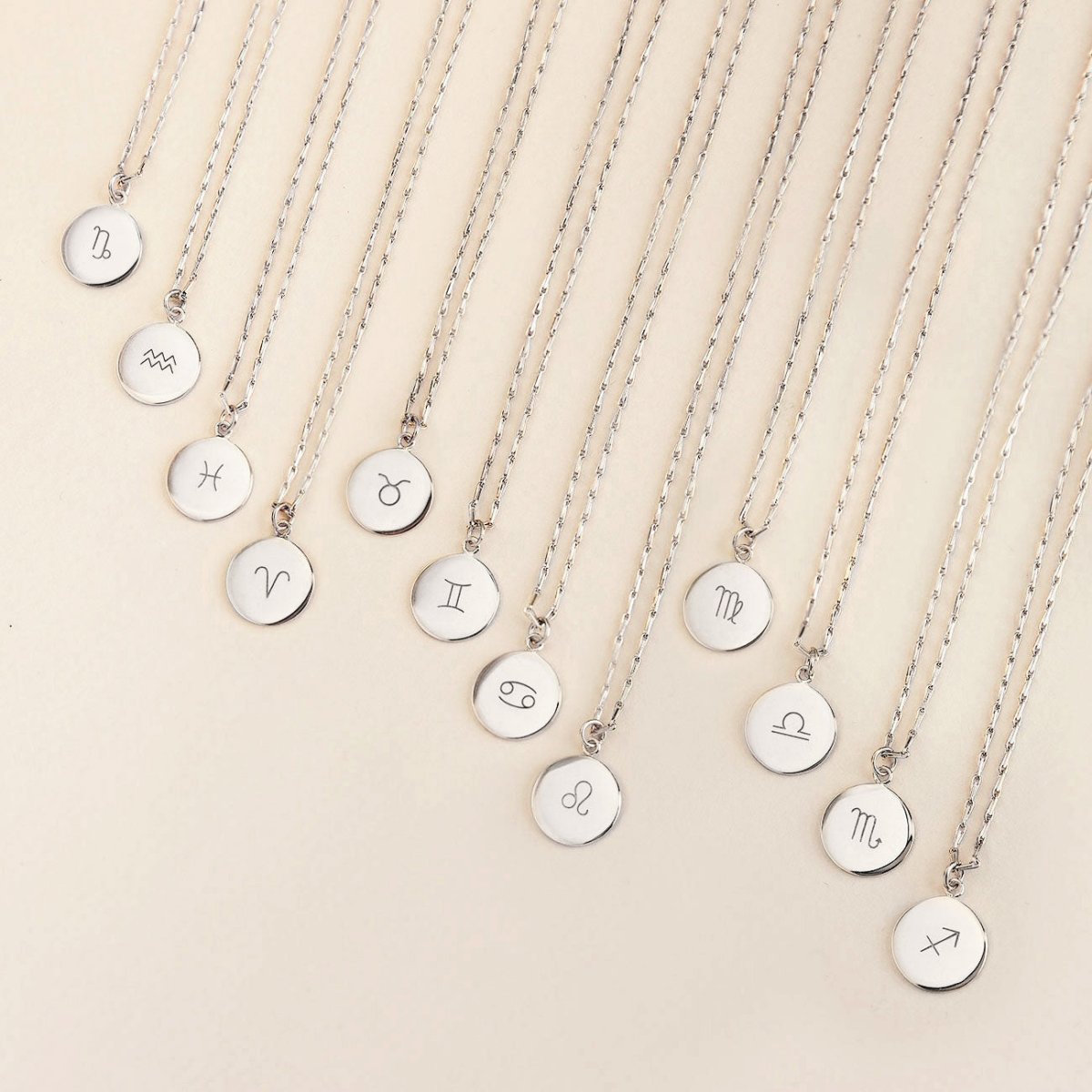 Sterling silver zodiac disc necklaces with engraved symbols fanned out on a cream background