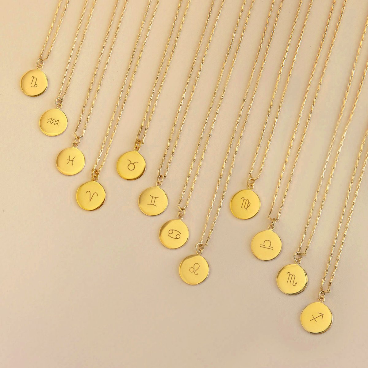 Gold vermeil zodiac disc necklaces with engraved symbols fanned out on a cream background