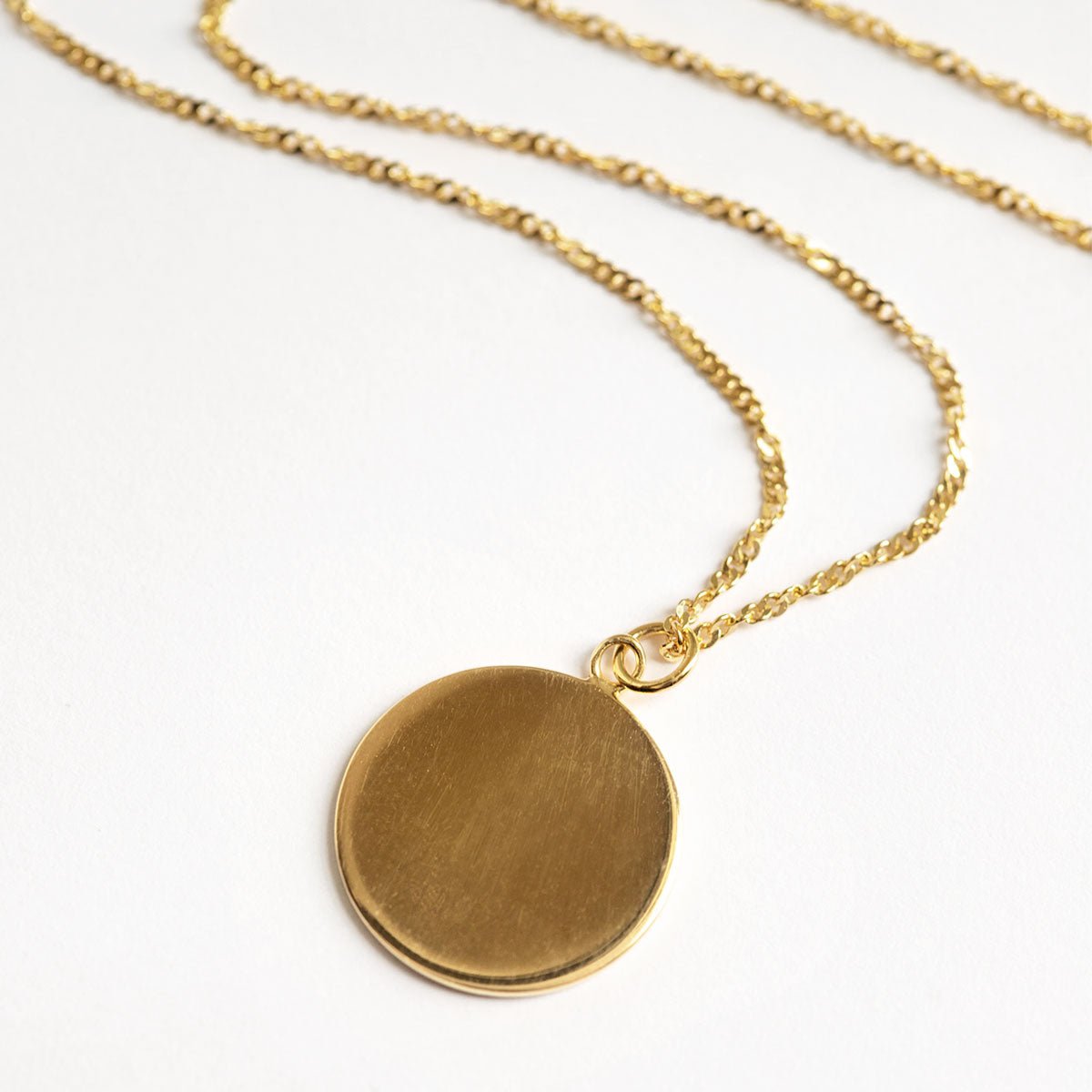 Gold vermeil round disc pendant on a twisted chain, laid on a white background