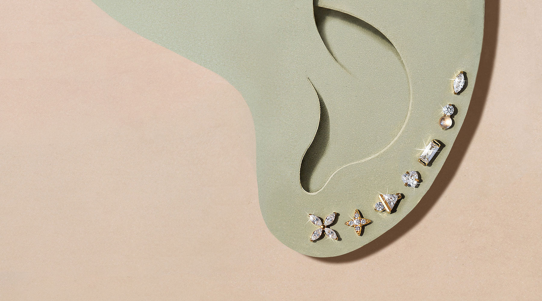 Green display ear on a beige surface set with a curved row of gold flower, baguette and crystal flat back studs