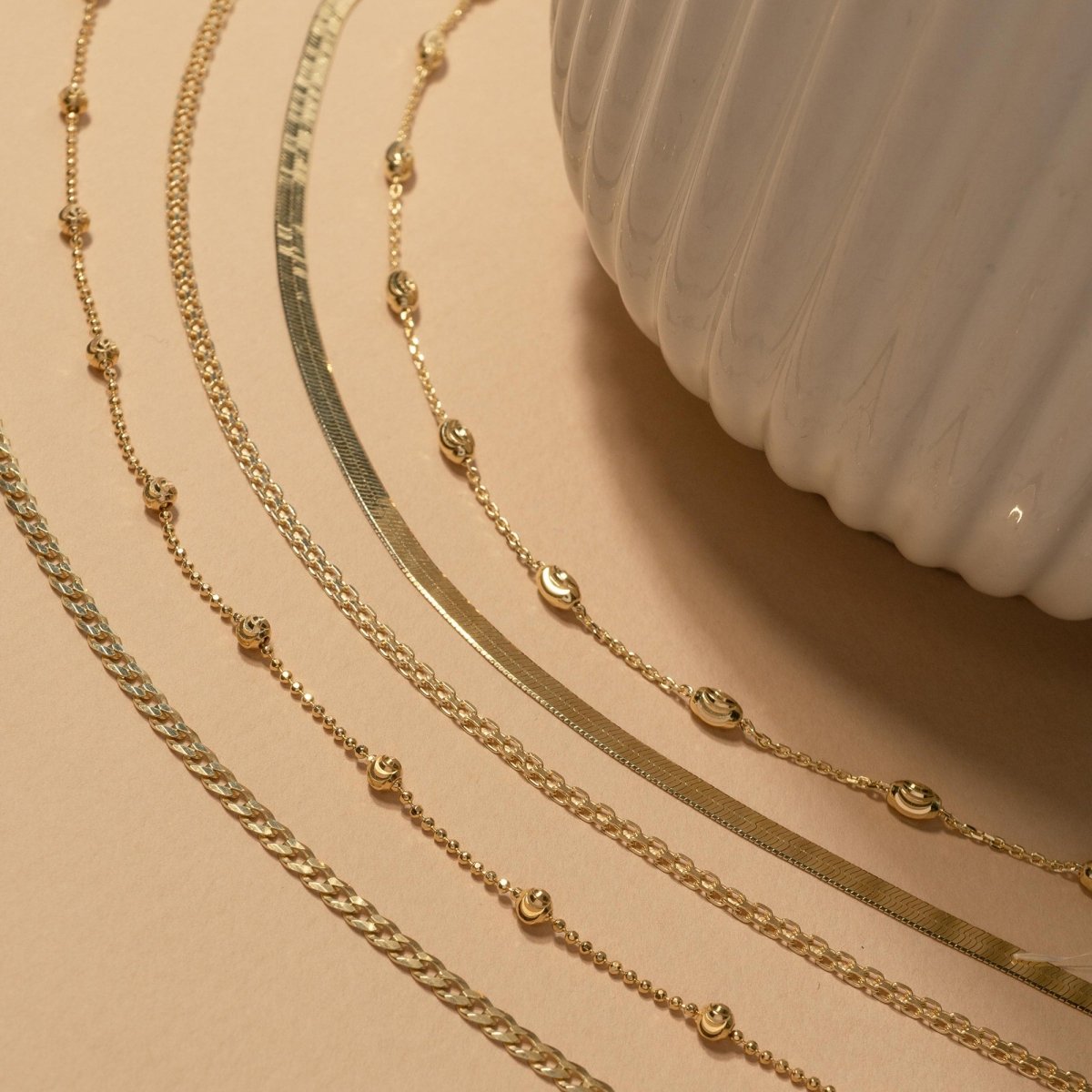 Gold vermeil Bismark chain anklet styled among assorted gold and silver chains on a cream background