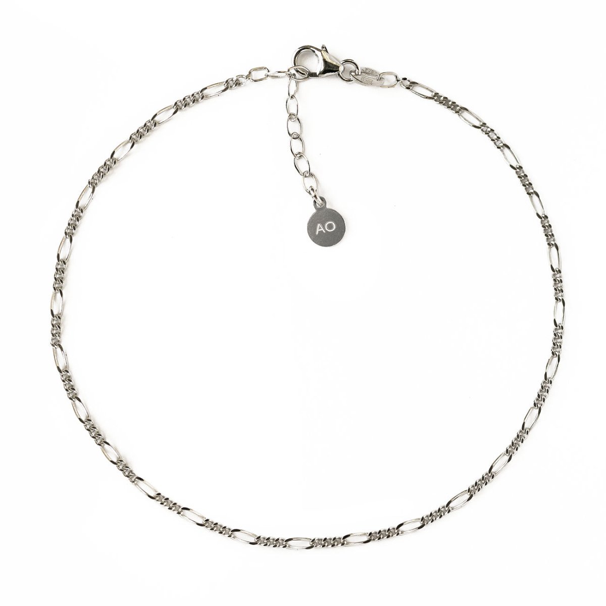 Sterling silver Figaro chain anklet with a lobster clasp and round logo tag, on a white background