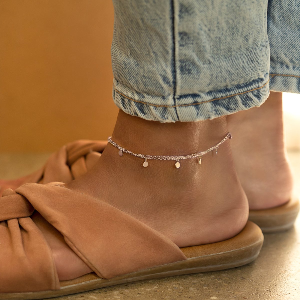 Sterling silver disc anklet shown on a model's ankle with jeans and tan sandals