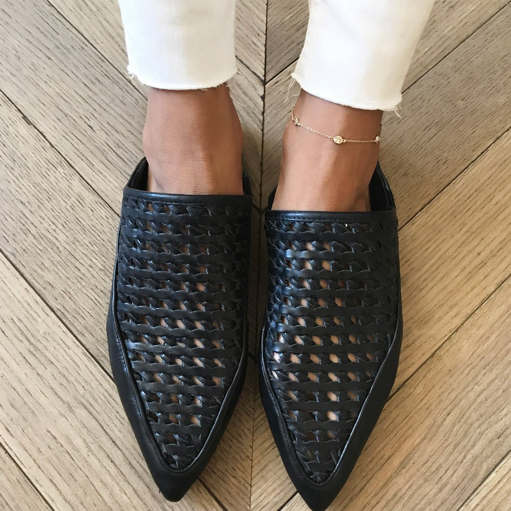 Gold station anklet shown on a model's ankle with white jeans and black woven flats