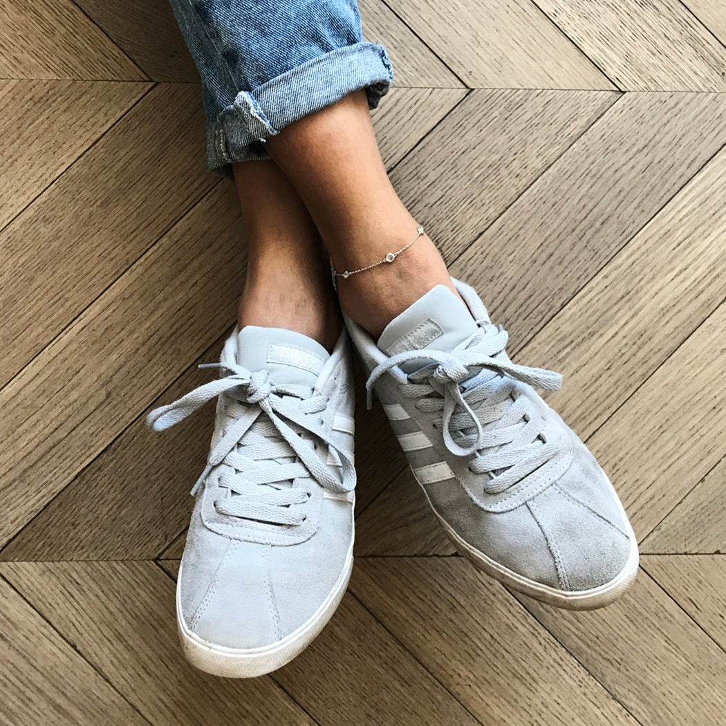 Silver station anklet on a model's ankle, worn with grey suede sneakers