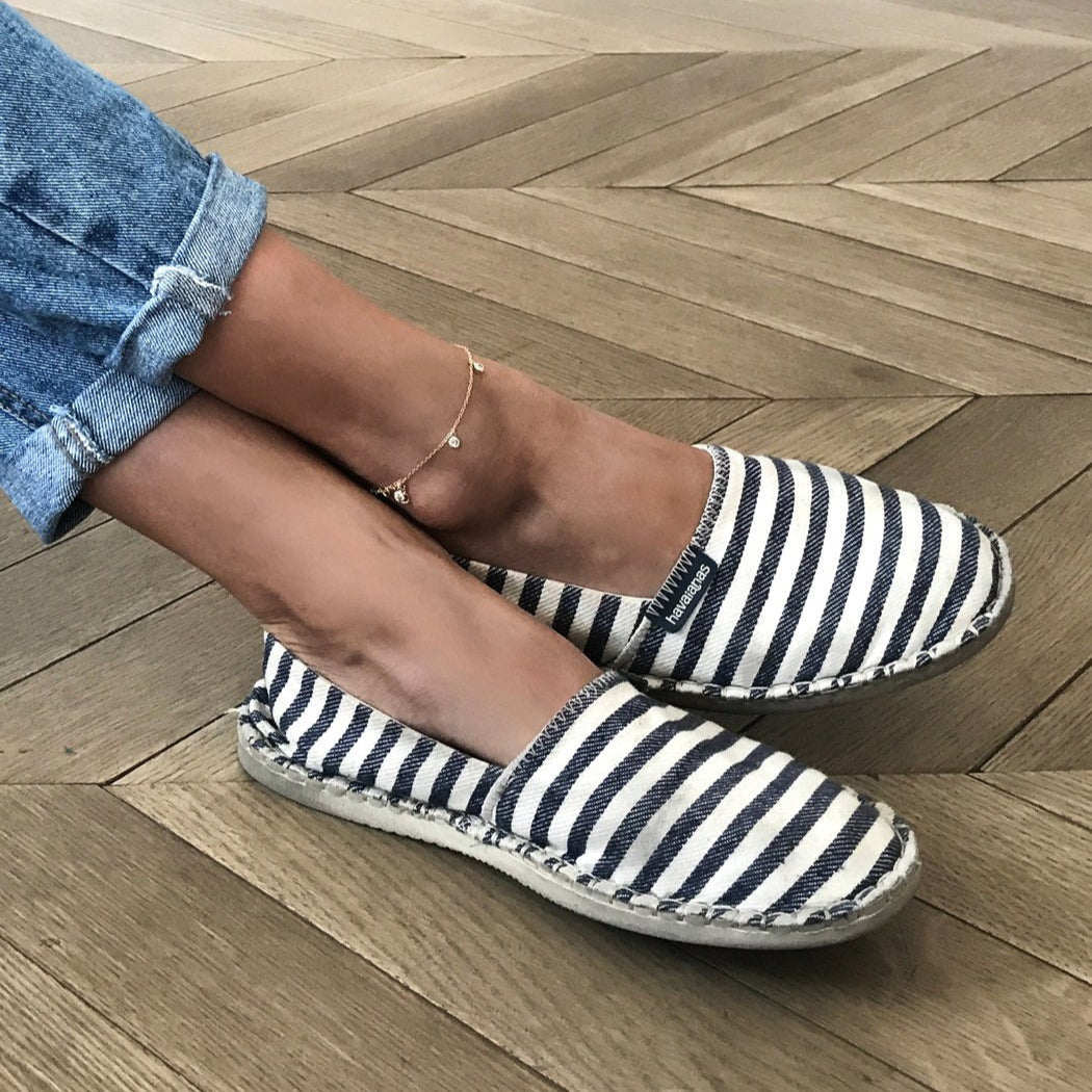 Gold vermeil clear-stone dangle anklet on a model's crossed ankles with striped espadrilles